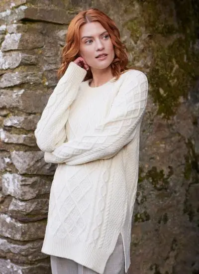 Red haired woman in abbey wearing white Aran sweater with arm folded looking to right